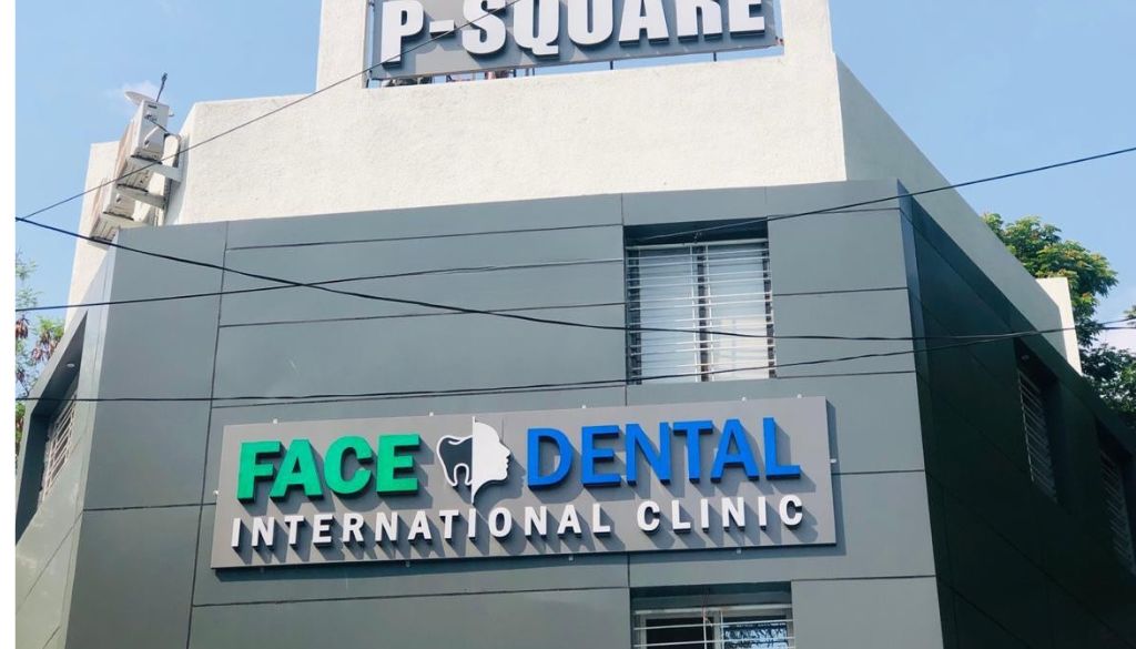 A modern dental office scene depicting an "Oral Cancer Screening Process" at Face N Dental Clinic. In the foreground, a dentist in professional attire attentively examines a patient seated in a dental chair, with a bright overhead light illuminating the scene. The dentist is holding a Velscan device, a sleek, high-tech screening tool, while the patient appears calm and relaxed. In the middle ground, dental instruments and a computer display with digital health records can be seen, suggesting a thorough examination process. The background shows a clean and inviting dental office with soothing colors and framed dental health education posters. Soft, natural lighting enhances the professional atmosphere, conveying trust and care in patient health.